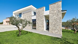 Une maison moderne à deux étages, dotée d’une façade en pierre, de grandes fenêtres et d’une pelouse bien entretenue.