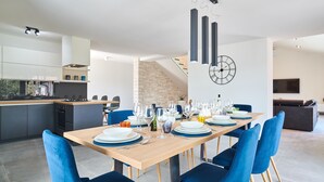 Un espace repas moderne avec une table en bois dressée pour six personnes, des chaises à l’assise rembourrée de couleur bleue, et une cuisine en arrière-plan.