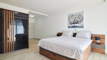 Ein modernes Schlafzimmer mit einem hölzernen Bettgestell, einem großen Fenster mit Vorhängen, einem Baumgemälde und einem Nachttisch mit einer Lampe.