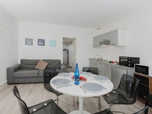 Una sala de estar moderna con un sofá gris, una mesa de comedor con sillas, una cocina con microondas y un mueble pequeño.