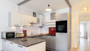 Uma cozinha moderna com armários brancos, uma ilha central, micro-ondas, cafeteira e backsplash vermelha.