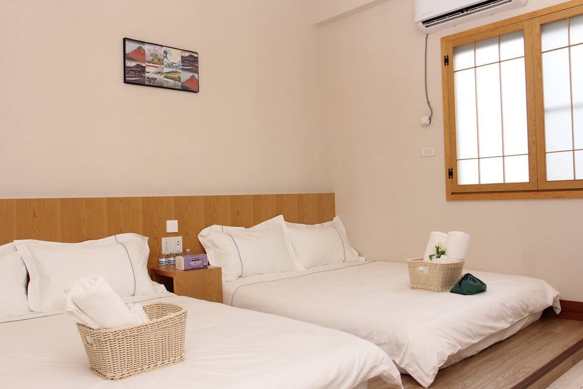 Une chambre d’hôtel avec deux lits, une tête de lit en bois, un climatiseur fixé au mur, une fenêtre avec vue et un tableau encadré accroché au mur.