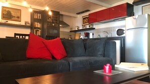 Une cuisine moderne avec des meubles rouges, un canapé noir avec des coussins rouges et un réfrigérateur en acier inoxydable.