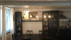 Un coin repas avec une table et des chaises en bois, une bibliothèque et un espace cuisine équipé d’une cuisinière et de placards.