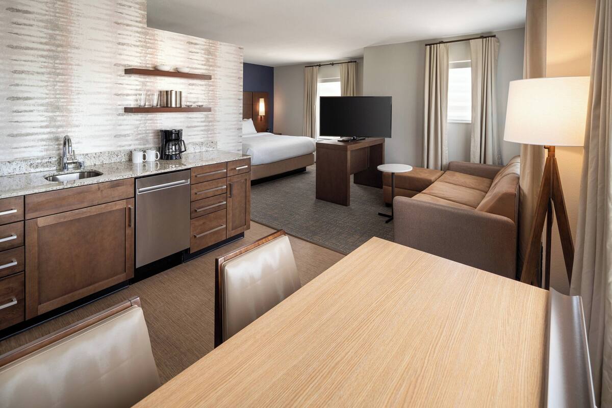 A hotel room with a kitchenette, a bed, a TV, a desk, and a seating area.