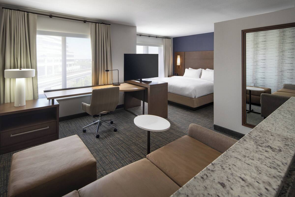 A hotel room with a bed, a desk with a chair, a TV, a small table, and a sofa.