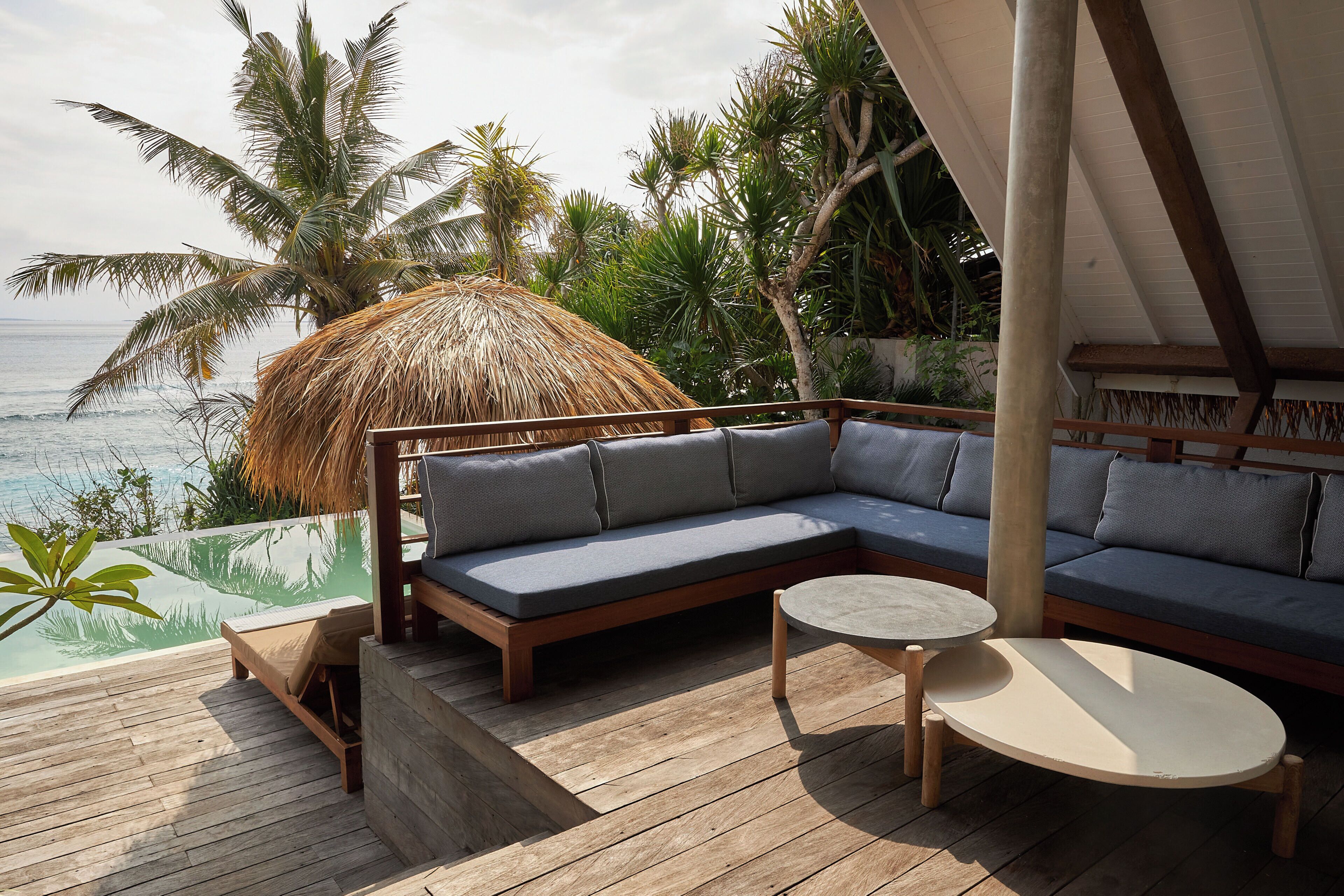 A wooden deck with a thatched-roof structure, a sofa, and a round table.
