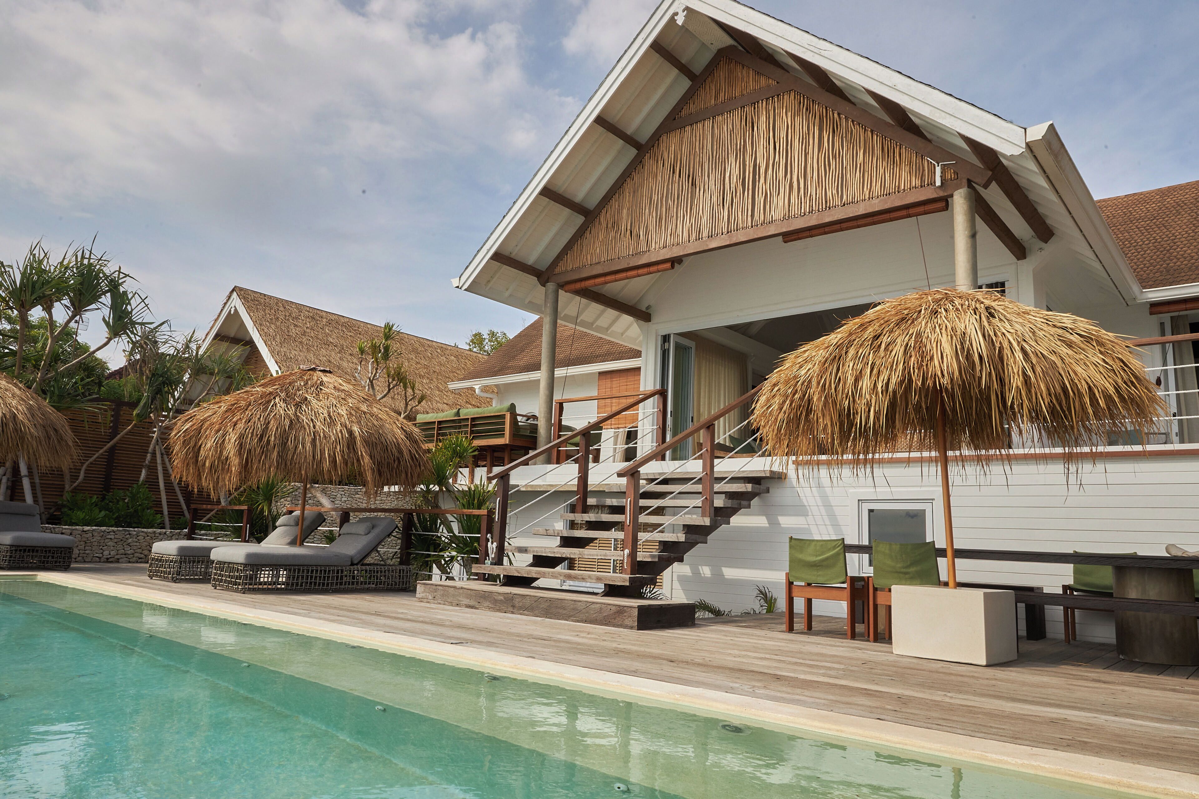 A resort with a swimming pool, lounge chairs, and a staircase leading to a covered area with a thatched roof.