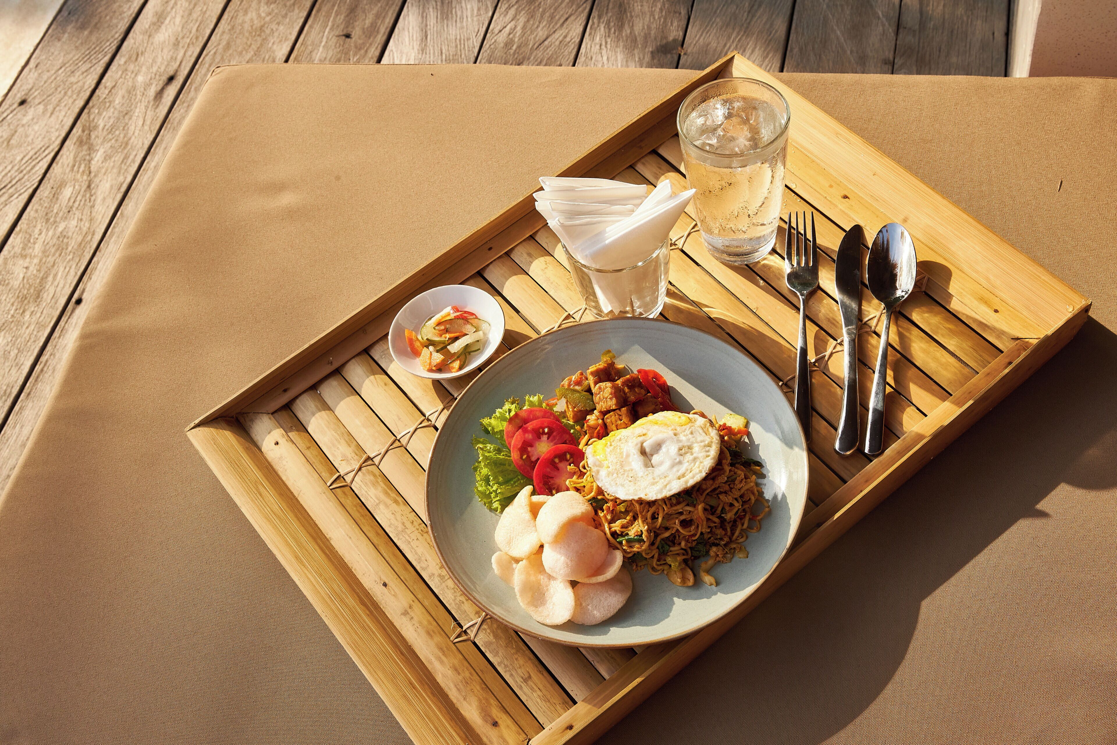A wooden table with a tray holding a plate of food, utensils, and a glass of water.