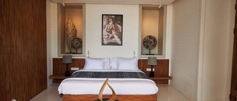 A modern bedroom with a large bed, wooden headboard, two bedside tables with lamps, a ceiling fan, and decorative wall art.