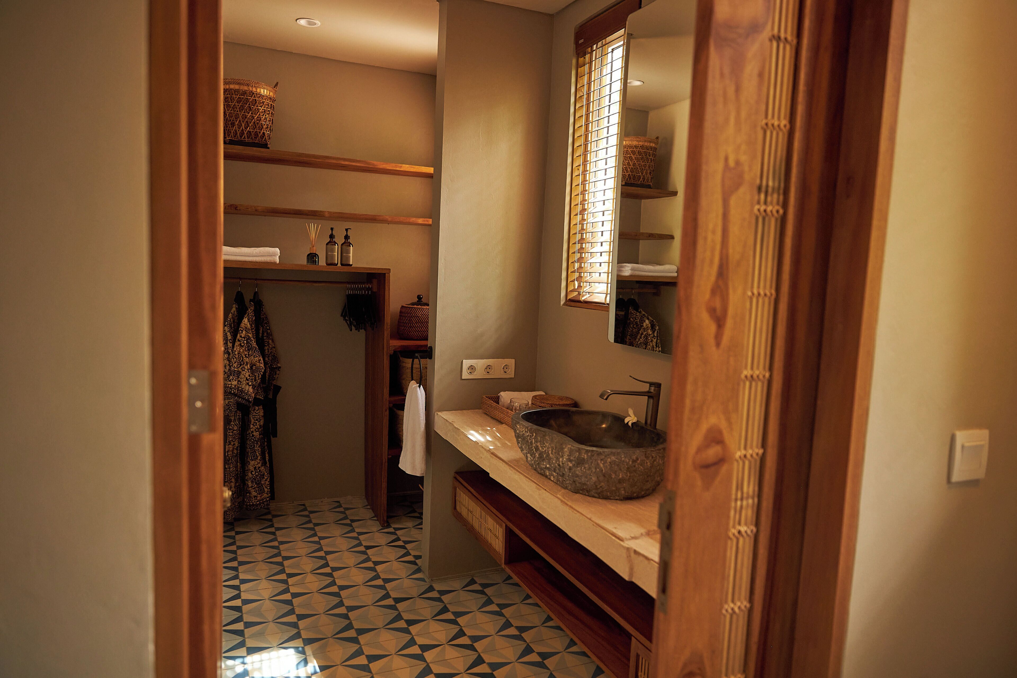 Ein Badezimmer mit geometrischen Fliesen, einem Holzkosmetikschrank, einem großen Spiegel und einem hängenden Handtuch.