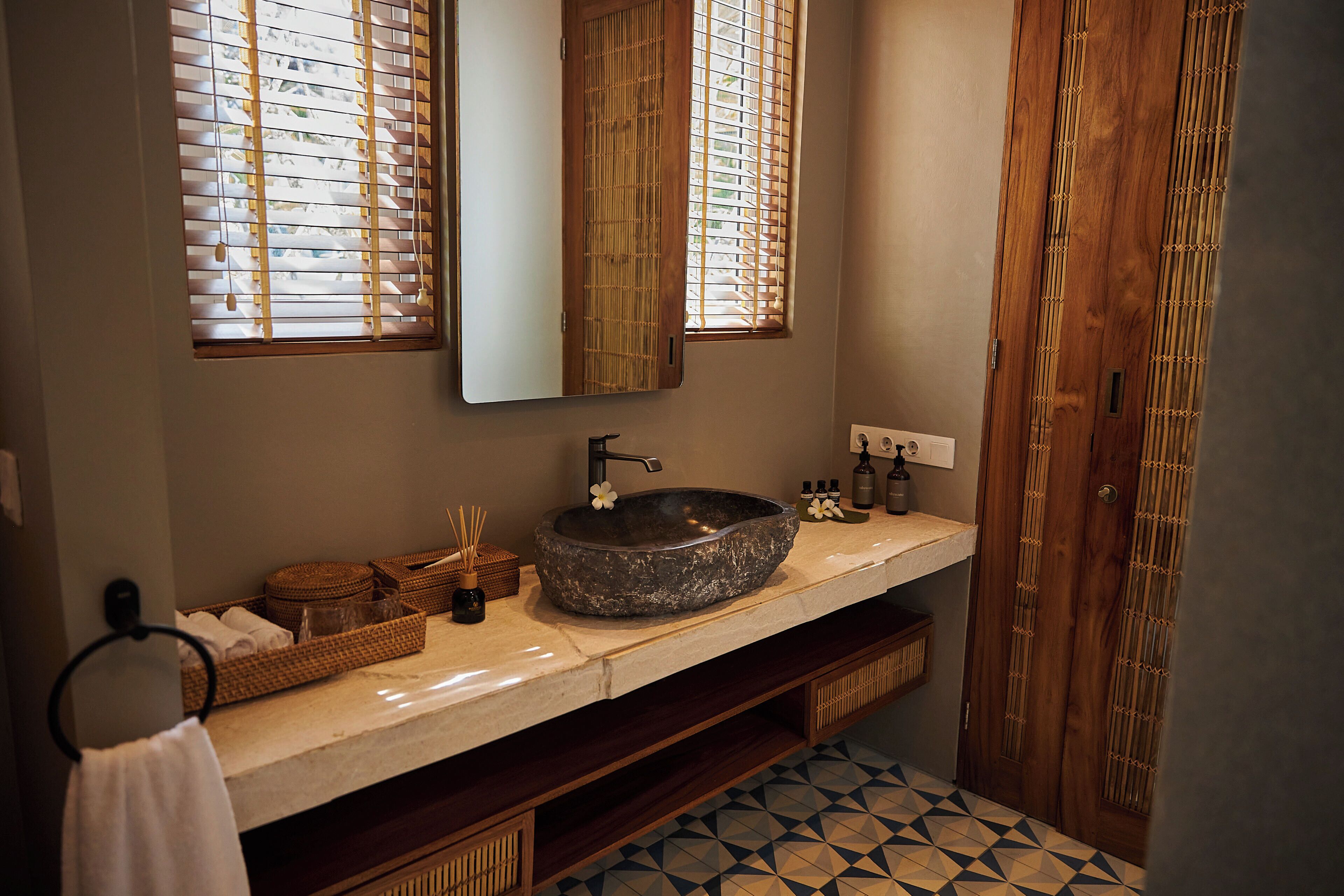 Un baño con un lavabo de piedra, tocador de madera y un espejo grande.