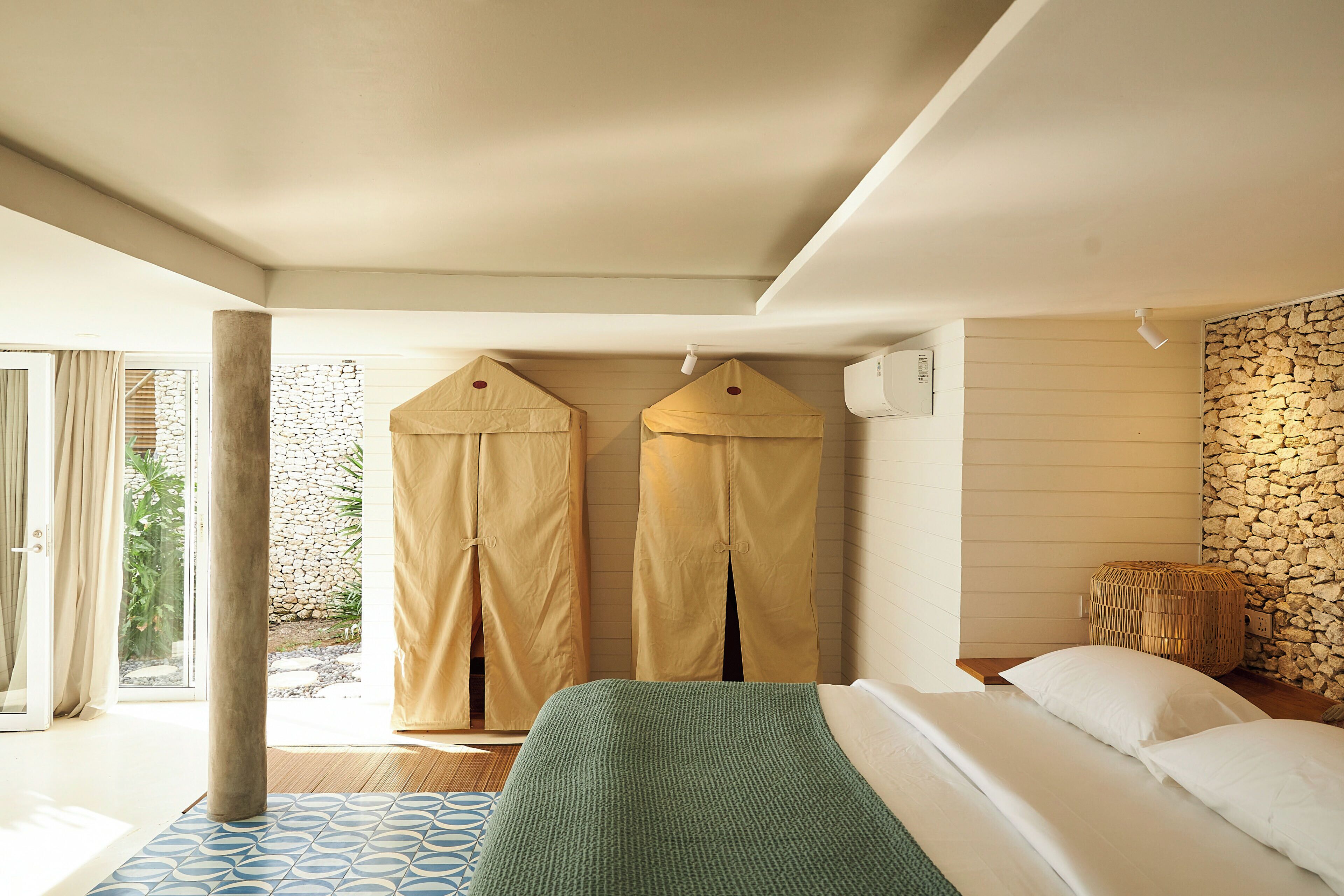 Une chambre à coucher avec un lit, une fenêtre, des rideaux, un mur en pierre et un panier en osier.