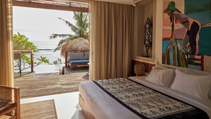 Een slaapkamer met een groot bed, uitzicht op het strand en een eethoek met een tafel en stoelen.
