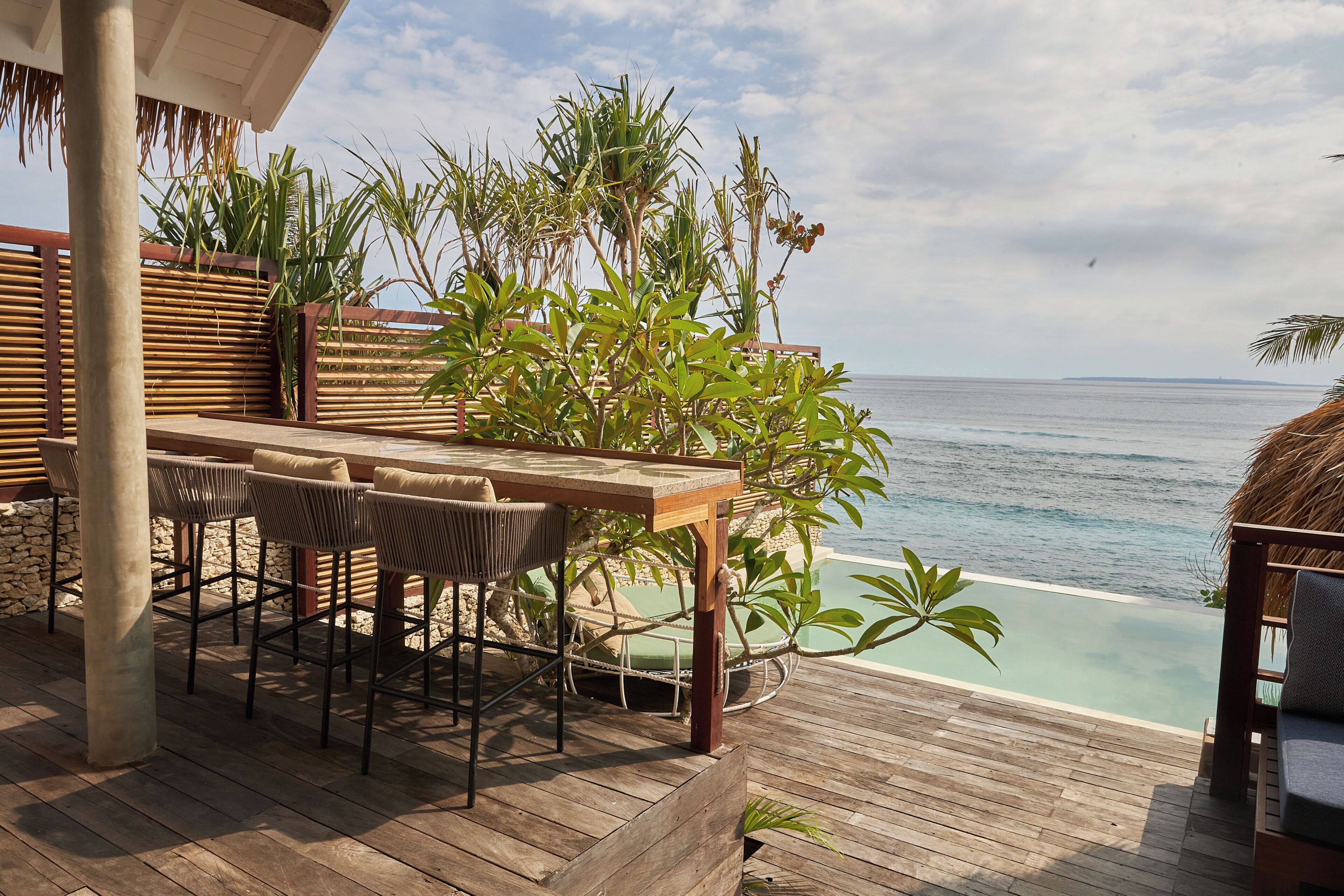 A wooden deck with a table and chairs, overlooking a clear blue sea.