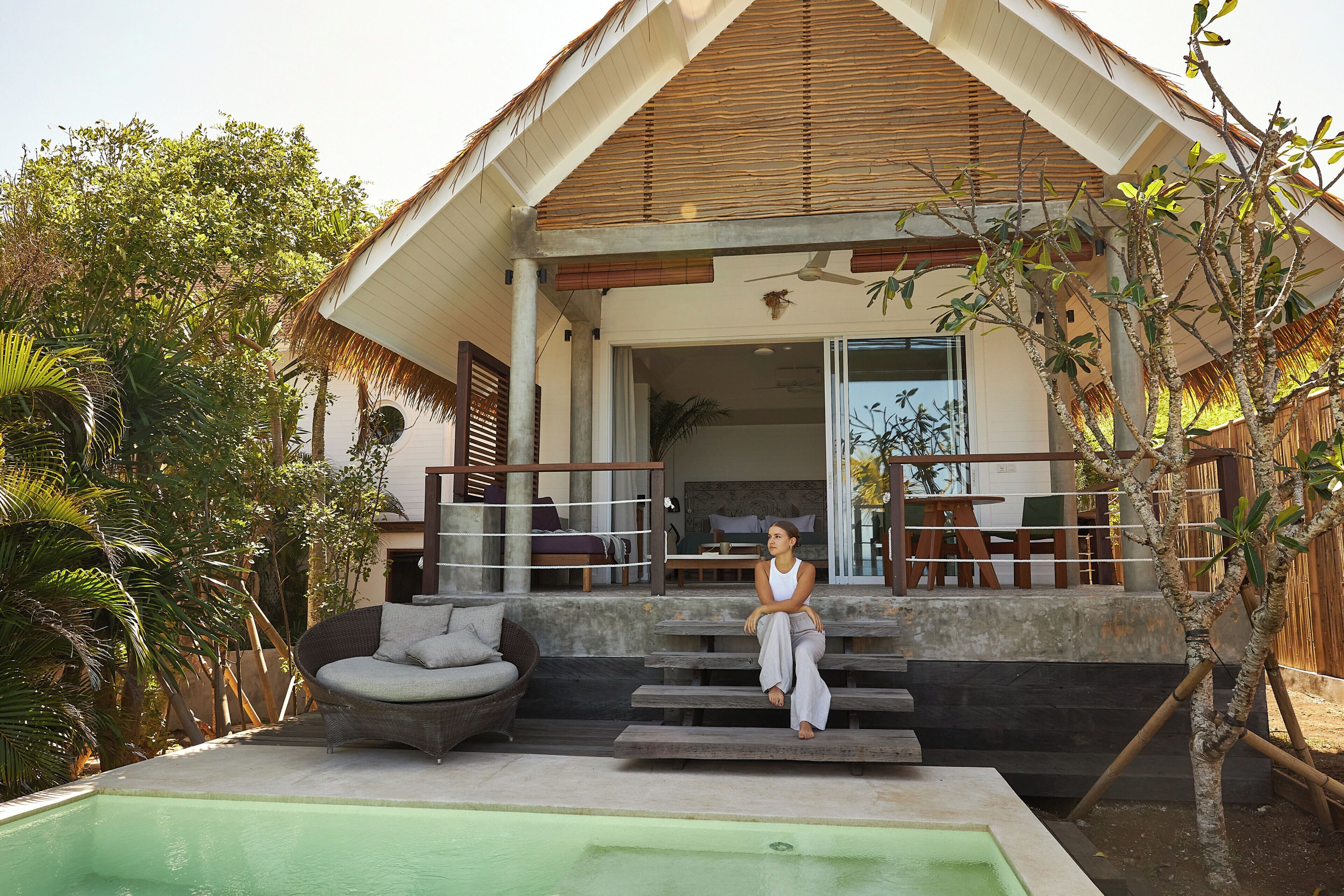 A modern house with a pool, outdoor seating, and a staircase leading to a deck.