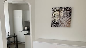 A modern living room with a white cabinet, a dining area with a table and chairs, and a kitchen visible through an archway. - Altstadtwohnung (Chur)
