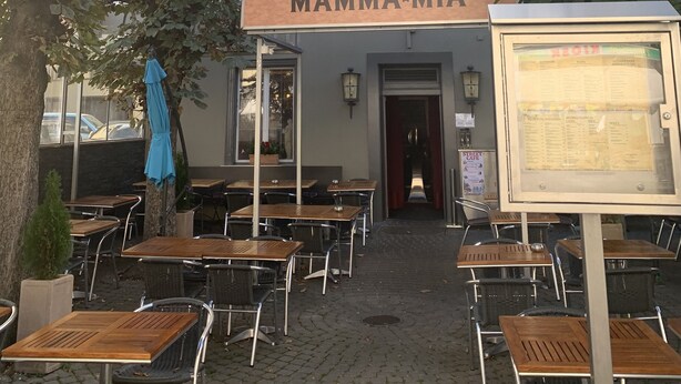 An outdoor seating area with tables and chairs, a sign for "RISTORANTE / PIZZERIA MAMMA-MIA", and a menu board. - Altstadtwohnung (Chur)