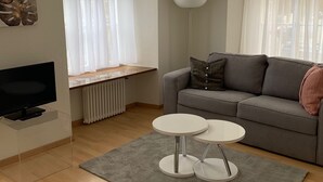 A modern living room with a grey sofa, a flat-screen TV on a glass stand, two white round tables, and a grey rug. - Altstadtwohnung (Chur)