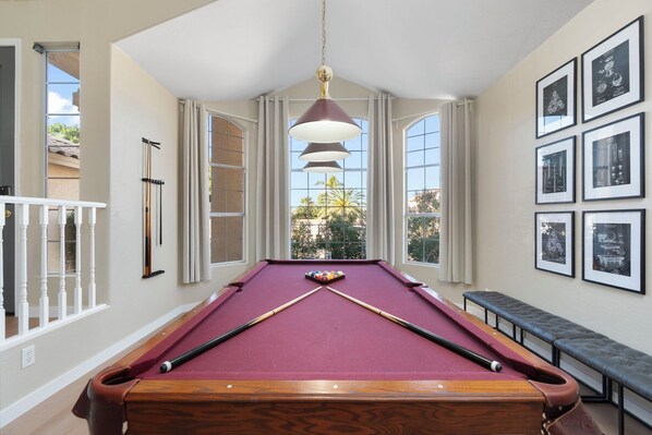 A pool table in a room with large windows, a hanging light fixture, and framed pictures on the wall. - BRAND NEW Spacious 5BR with Heated Pool & Hot Tub & Mini Putt (Mesa)