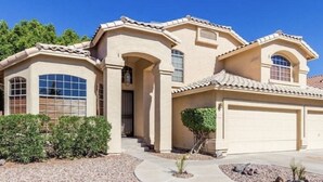 A two-story house with a beige facade, large windows, and a garage. - Brand New Luxury 5BR | Pool, Hot Tub & Mini Golf (Mesa)
