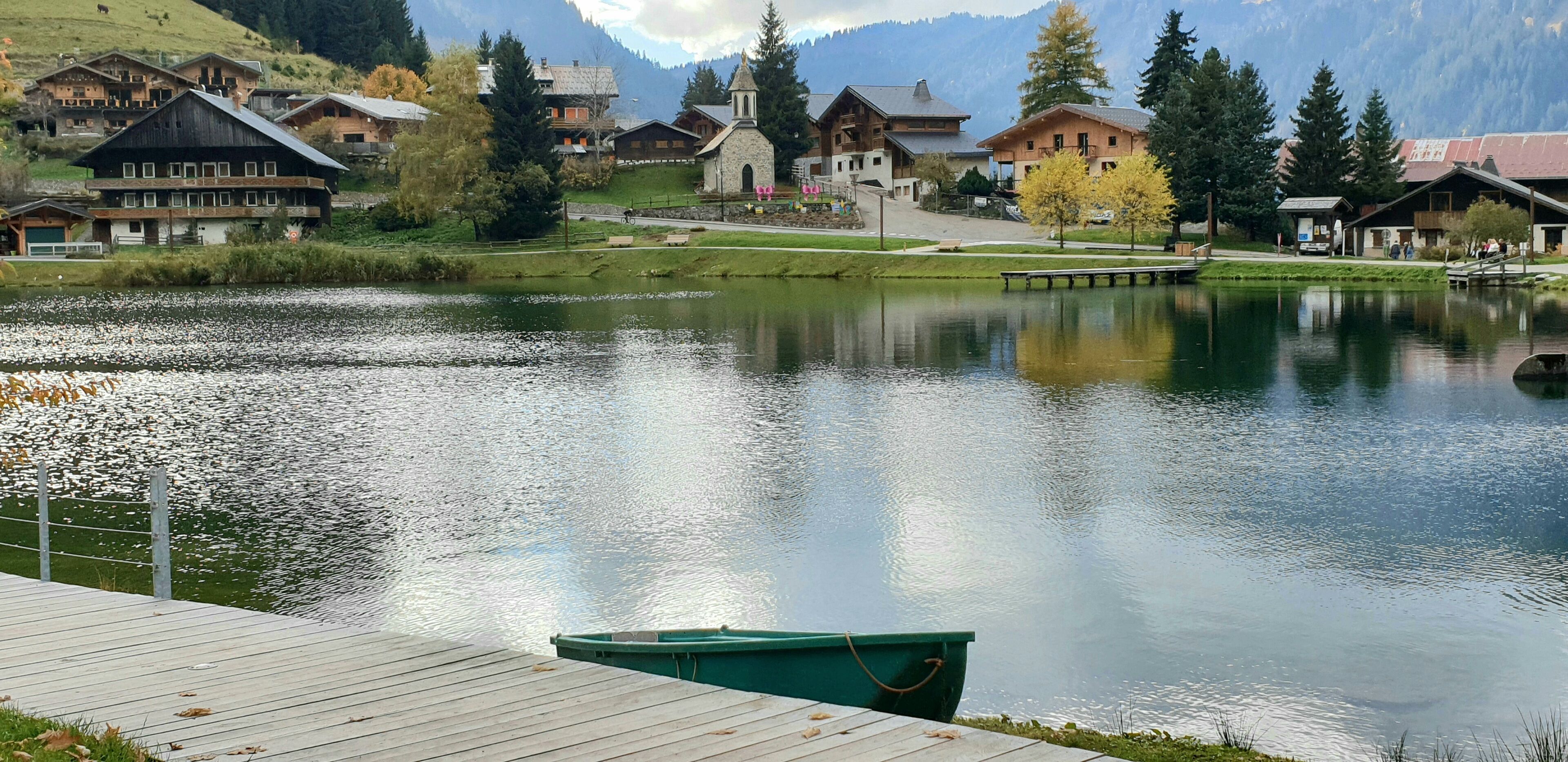 A serene lakeside village with traditional wooden houses, a small church, and a dock with a boat.