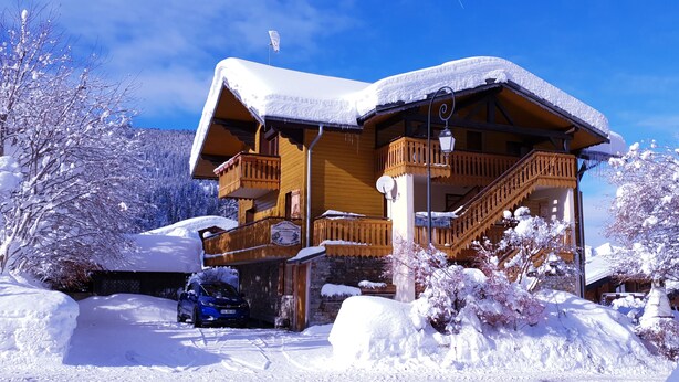 Eine Holzhütte mit Balkon, umgeben von schneebedeckten Bäumen und einem geparkten Auto.