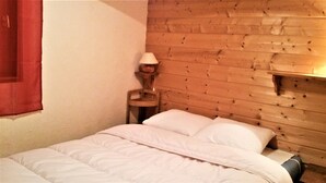 Ein Zimmer mit hölzernem Kopfteil, einem Bett mit weißer Bettwäsche, einem kleinen Nachttisch mit Lampe und einem roten Vorhang.