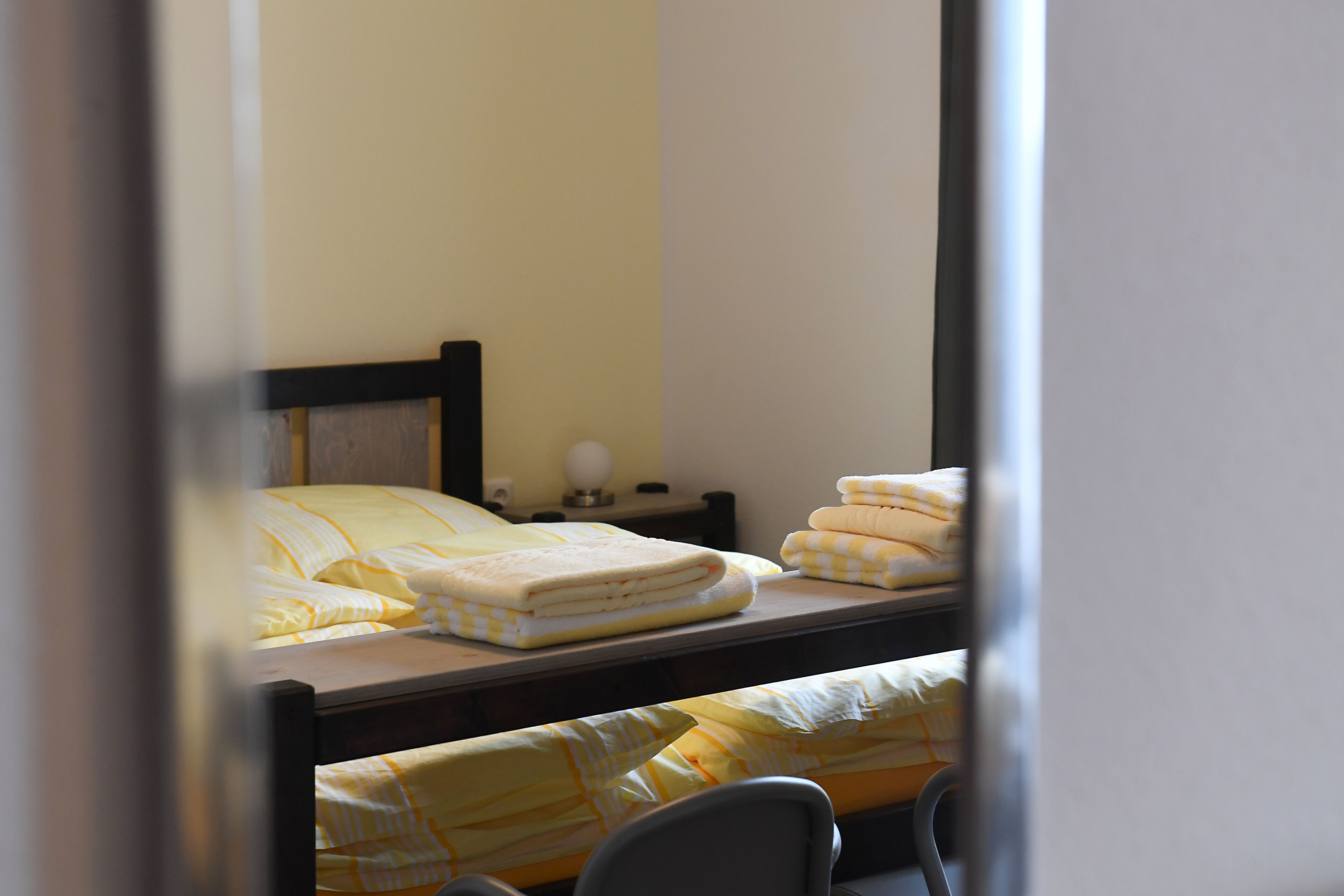 A single bed with a wooden headboard, a bedside table with a lamp, and neatly folded blankets.