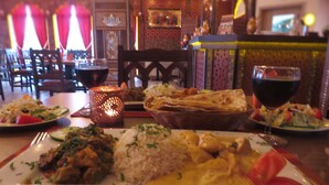 Un ambiente de restaurante con una mesa preparada para una comida, incluyendo platos de comida, una copa de vino tinto y una vela encendida.