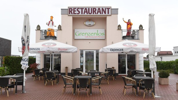 Un restaurante llamado Grenzenlos con terraza y dos estatuas en el balcón.
