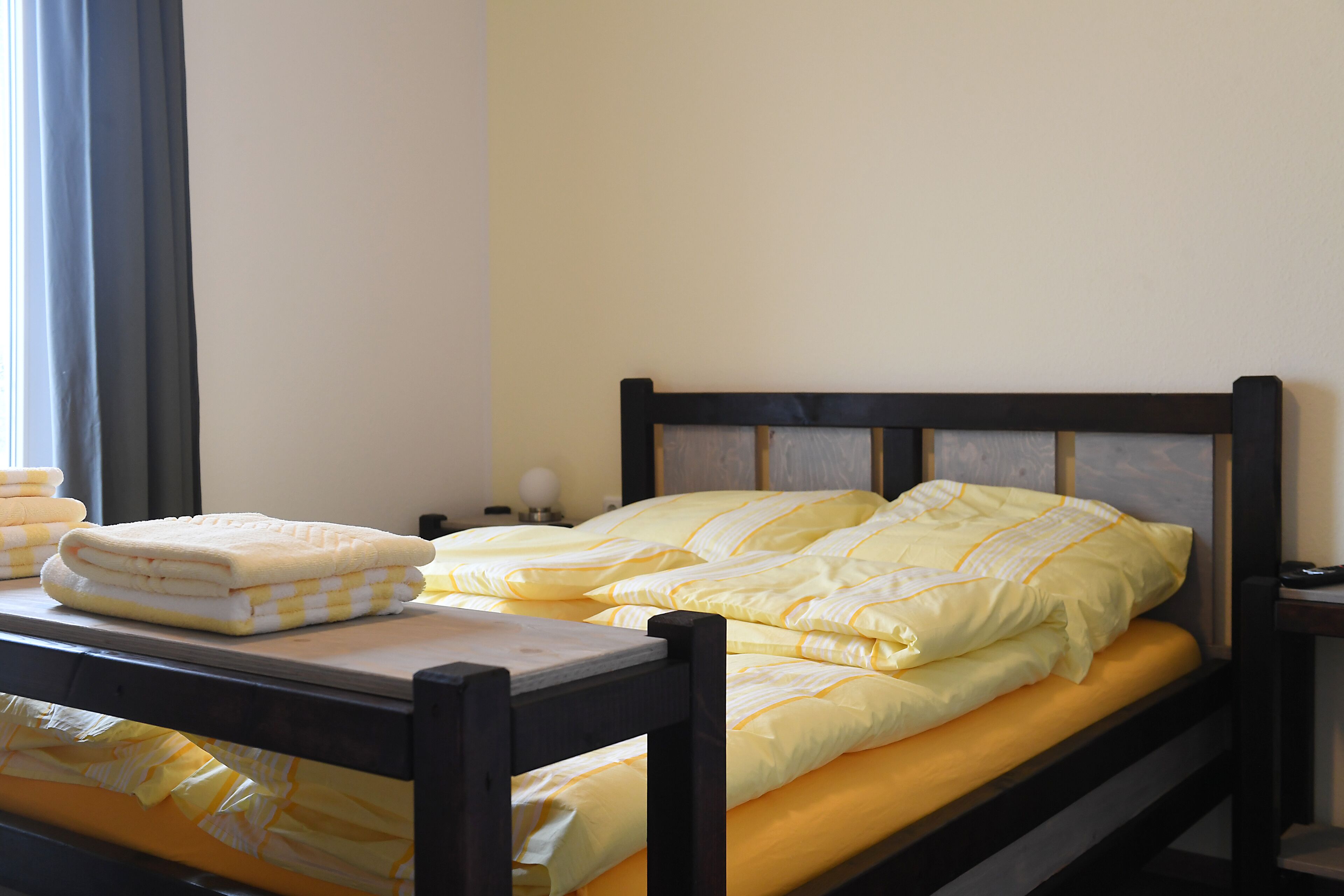 Una cama bien hecha con ropa de cama amarilla y un cabecero de madera en una habitación con un diseño sencillo y limpio.