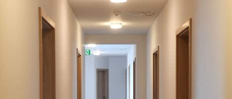 A long, narrow hallway with wooden doors on both sides, a green emergency exit sign, and a light fixture on the ceiling.