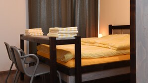 Una cama individual con una colcha amarilla y un cabecero de madera. Hay una silla a la izquierda de la cama y una pila de toallas dobladas sobre el cabecero.