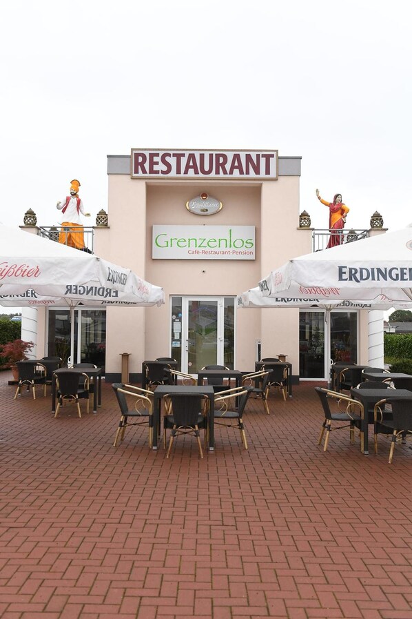 Un restaurante con mesas al aire libre, un letrero que dice "RESTAURANT" y el nombre "Grenzenlos" en la fachada.