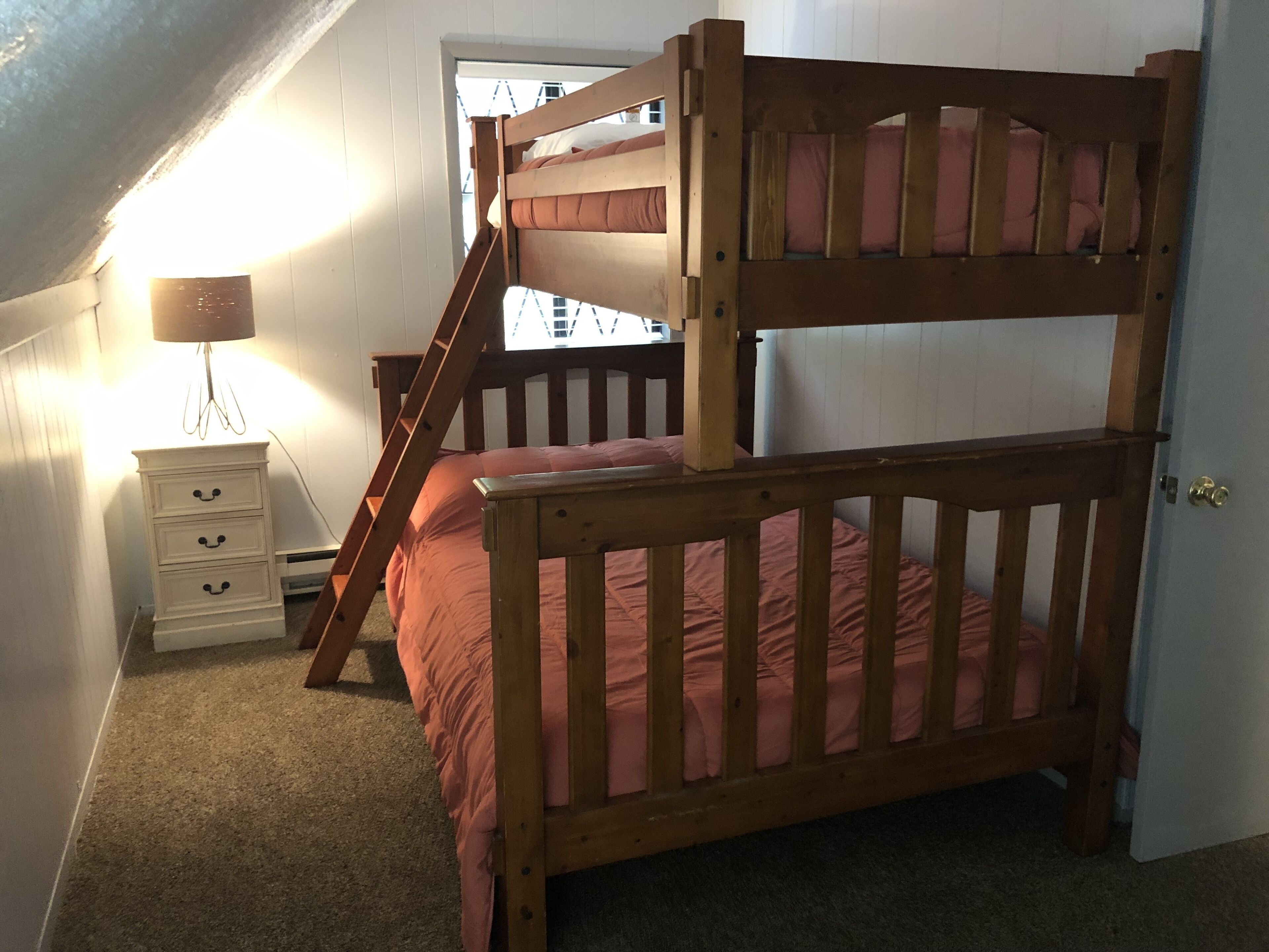 Una cama litera con escalera, una mesita de noche con lámpara y un aparador.