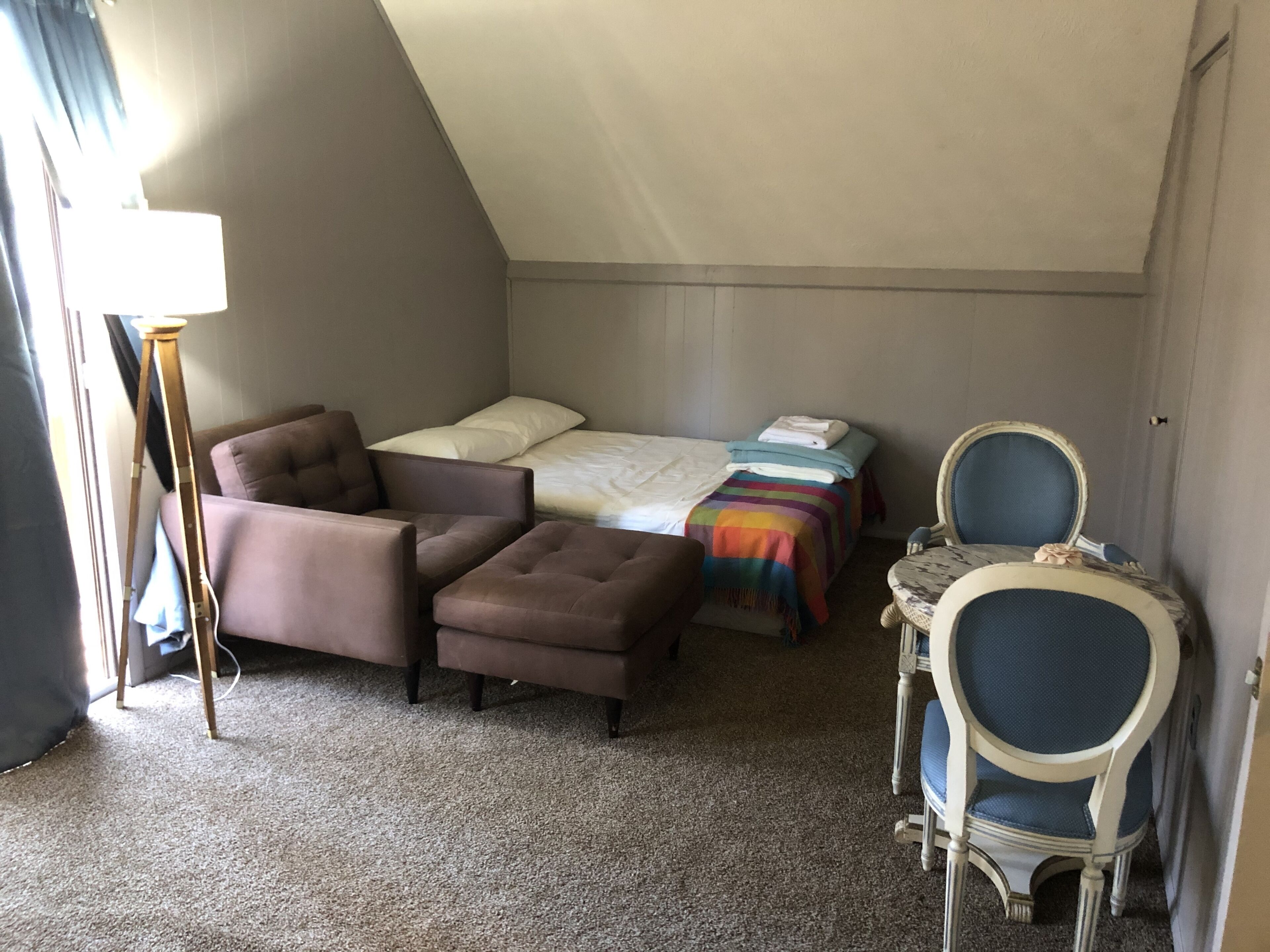A compact room with a bed, a sofa, a small table with a chair, and a floor lamp.