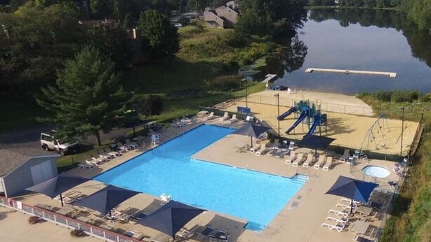 A swimming pool with adjacent sun loungers and a small slide, surrounded by trees and a calm lake. - Facilities all year round (Bushkill)
