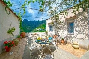 A patio with a round table and chairs, surrounded by potted plants and a view of mountains. - Il Mandorlo (Tramonti)