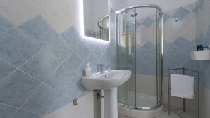 A bathroom with a glass-enclosed shower, a sink with a mirror above it, and a towel rack. - Il Mandorlo (Tramonti)