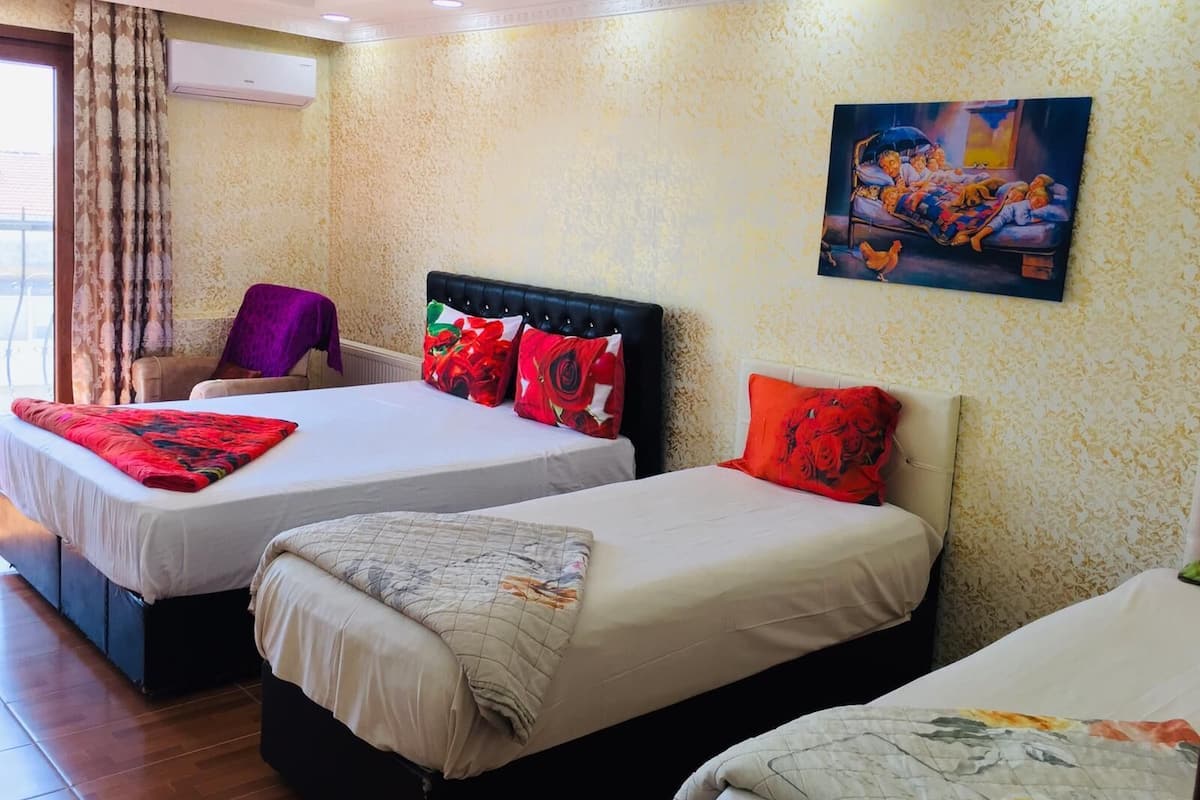 A hotel room with two beds, a chair, a painting on the wall, and a window with curtains.
