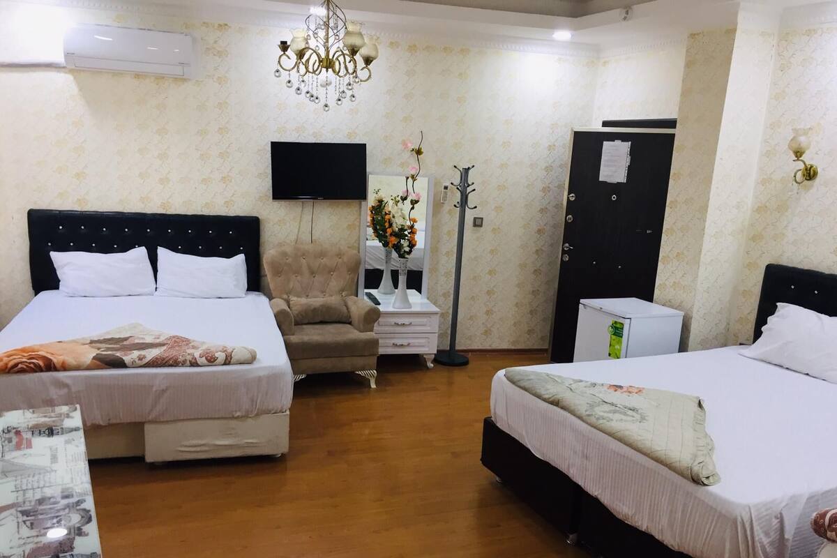 A hotel room with two beds, a TV, a chandelier, a desk, and a wardrobe.