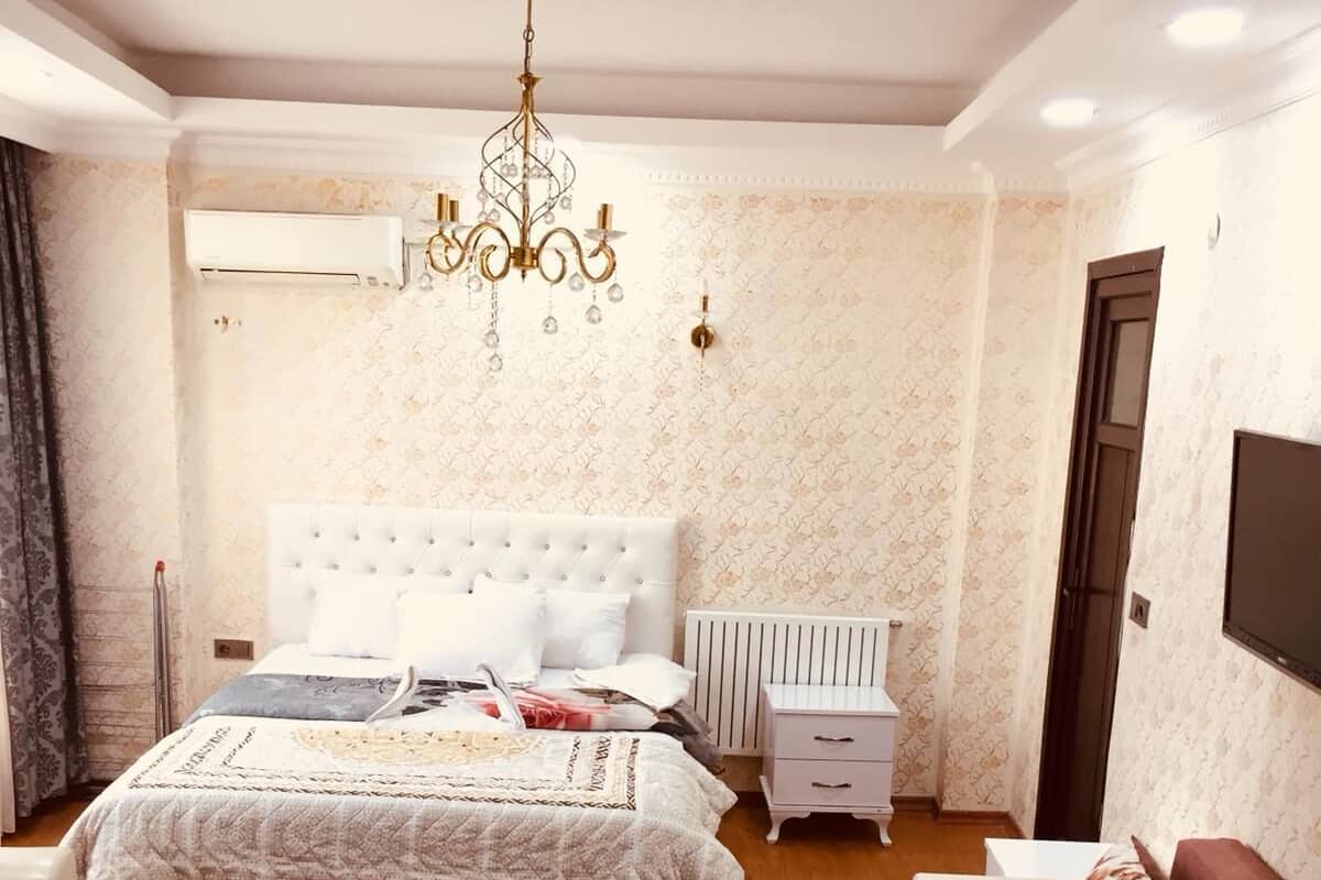 A bedroom with a large bed, a chandelier, a white dresser, and a brown sofa.