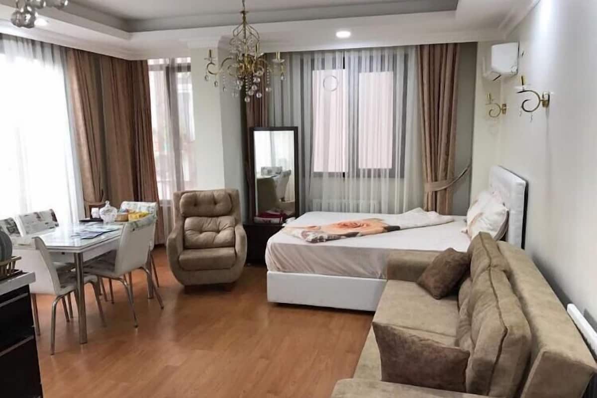 A hotel room with a bed, a desk, a chair, a sofa, and a chandelier.