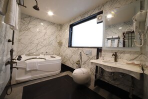 A modern bathroom with a marble wall, a large mirror, a bathtub, a toilet, and a sink. - HOTEL OPTIONS (Shahpura)