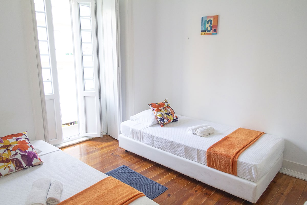 A room with two single beds, a wooden floor, a white door, and a small wall-mounted picture.