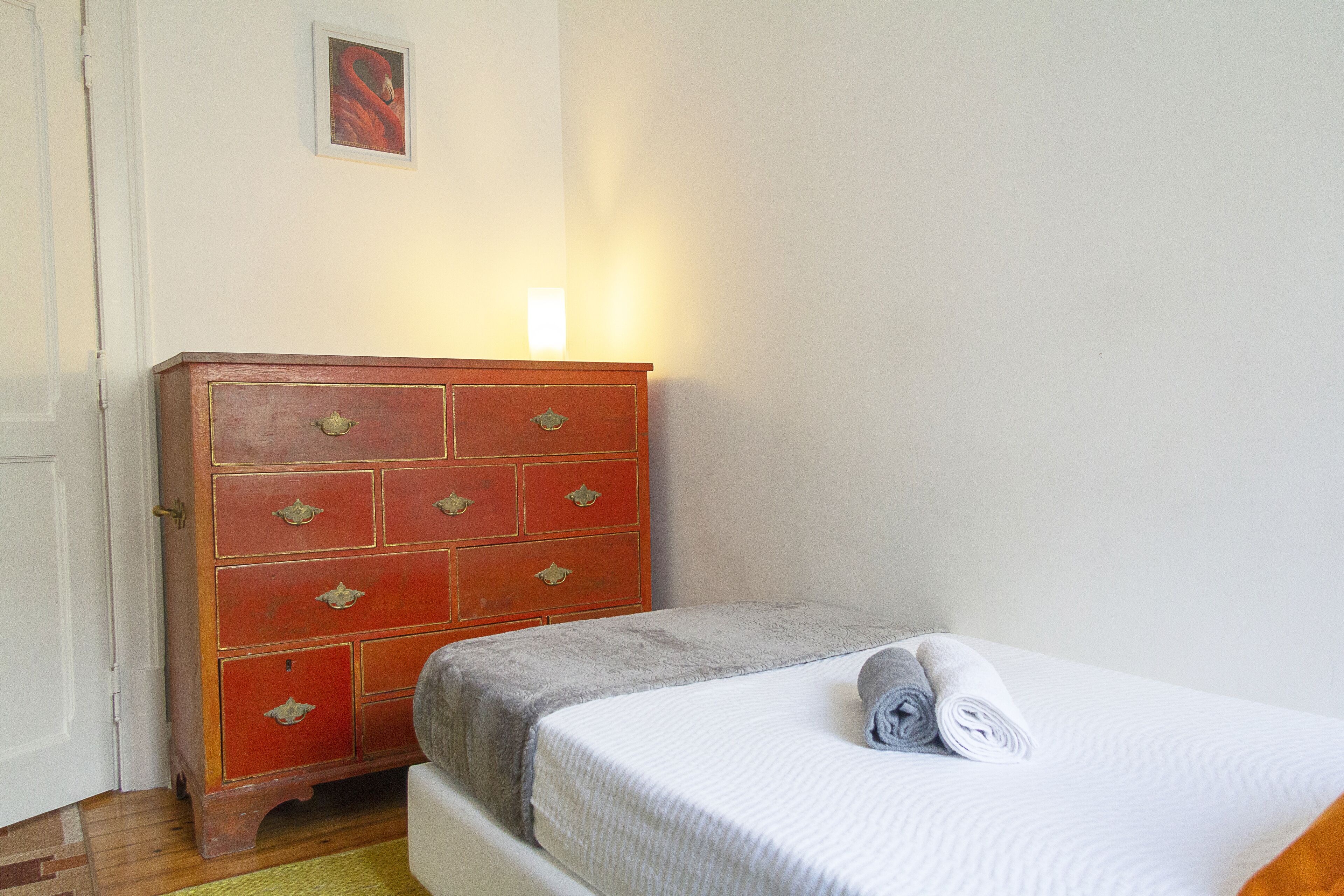 A bedroom with a bed, a wooden dresser, and a painting on the wall.