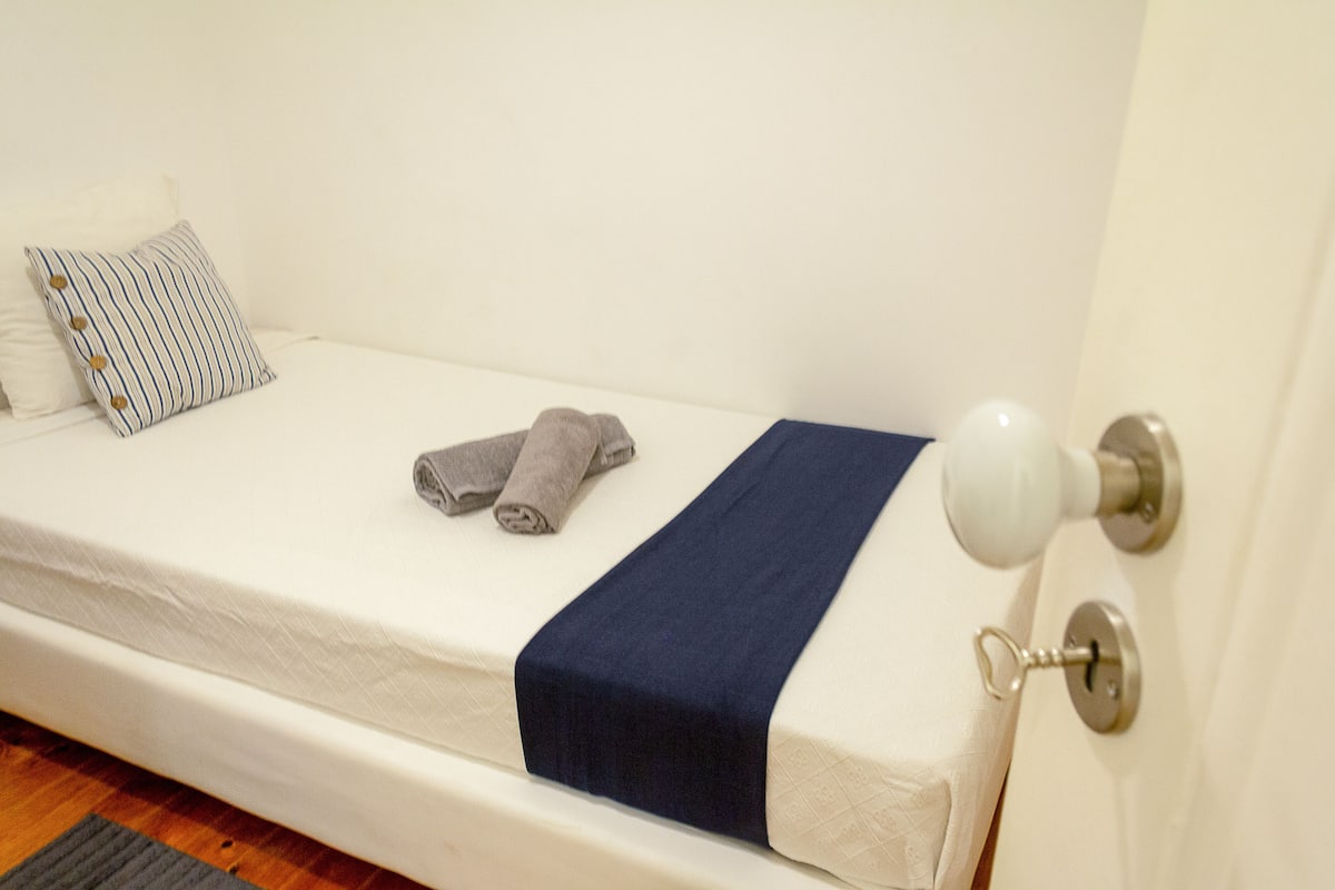 A single bed with a white mattress, a blue blanket, and a striped pillow.