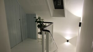 A staircase with a white railing, a potted plant, and a light fixture on the wall. - Katrinelund Bed and Breakfast (Tikob)