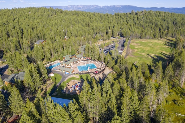 An aerial view of a resort with a swimming pool, guest cabins, and a large forested area.